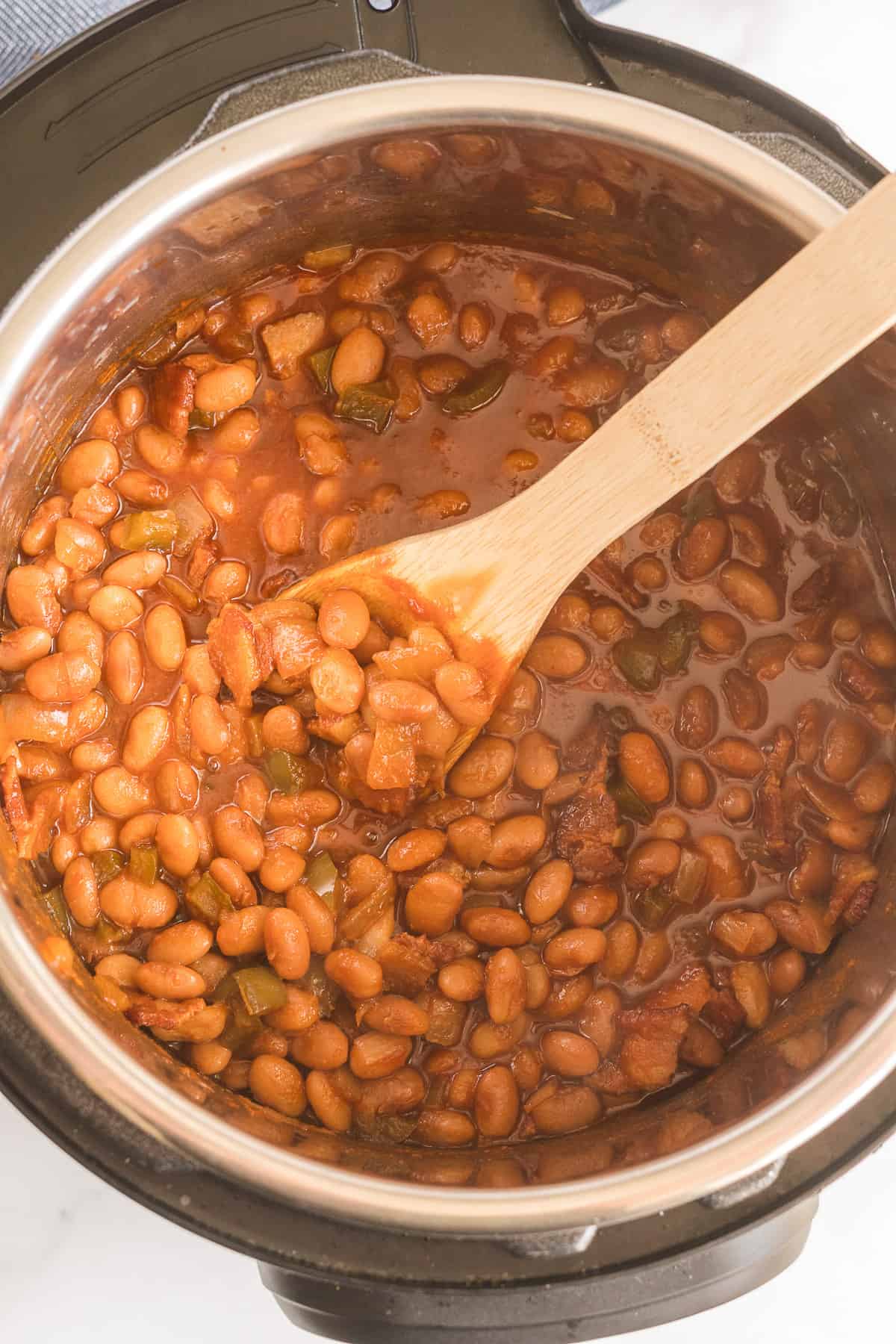 A wooden spoon stirs the baked beans in the Instant Pot.
