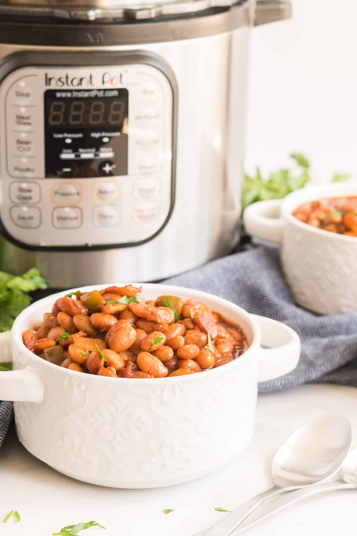 A white serving dish filled with baked beans sits in front of an Instant Pot.