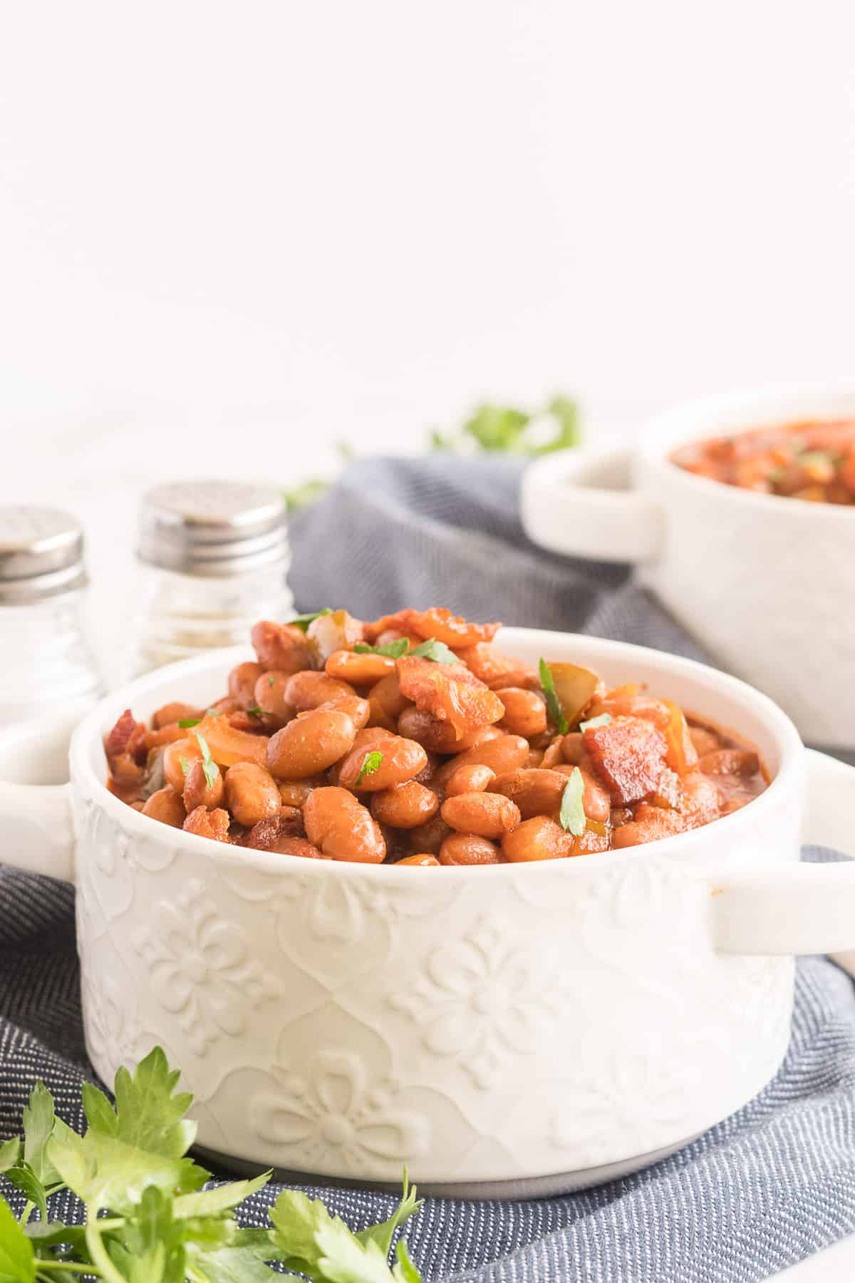 Baked Beans in a white serving dish with a blue cloth underneath.