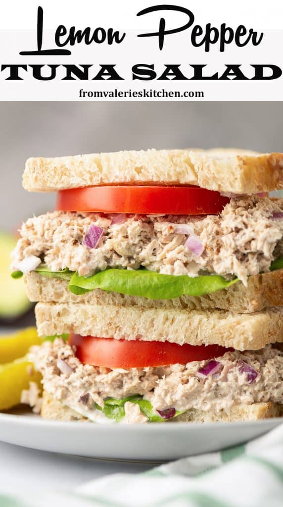 A tuna sandwich with tomato and lettuce cut in half and stacked on a plate.