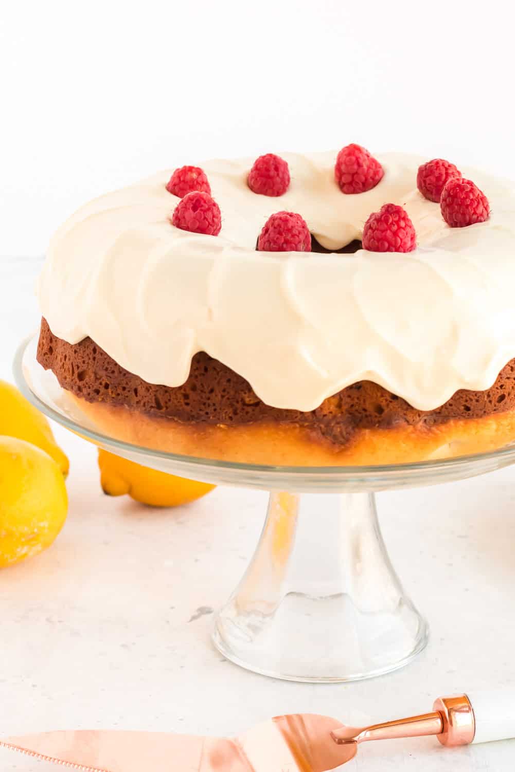 Lemon Raspberry Bundt Cake with Lemon Cream Cheese Icing on a glass pedestal cake plate with fresh raspberries on top.