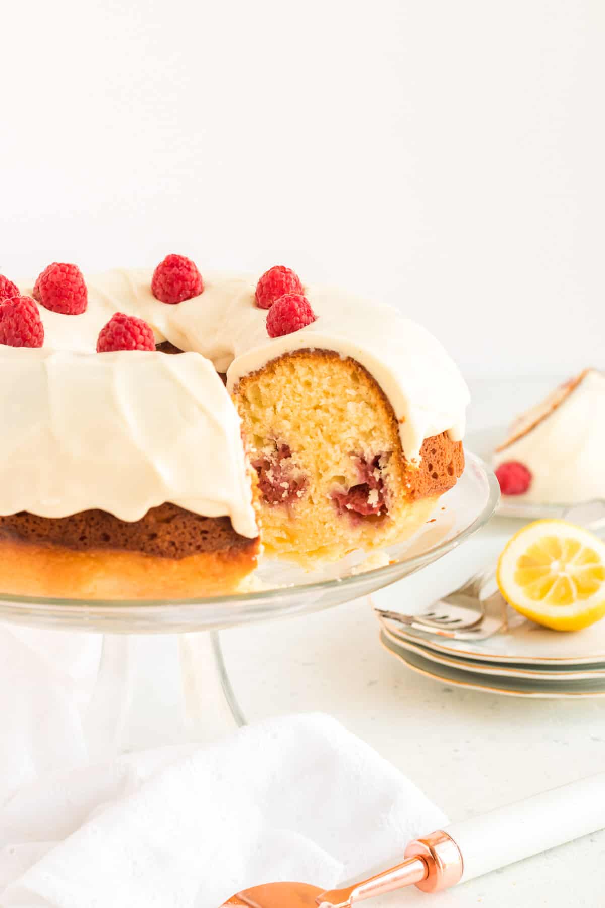 The Bundt cake on a glass pedestal cake plate with a fresh lemon in the background.