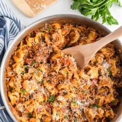 An overhead shot of the tortellini in a skillet with a wooden spoon.