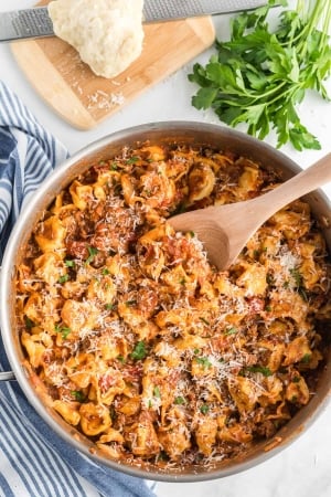 An overhead shot of the tortellini in a skillet with a wooden spoon.