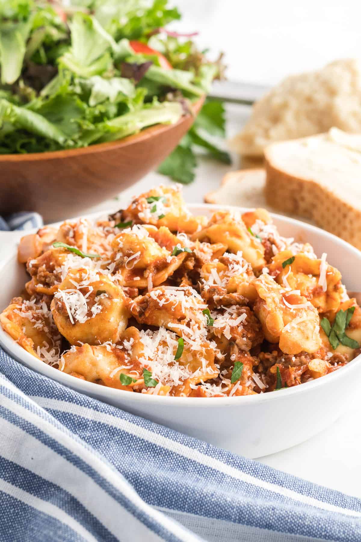 A white serving bowl filled with meaty tortellini with a green salad in the background.