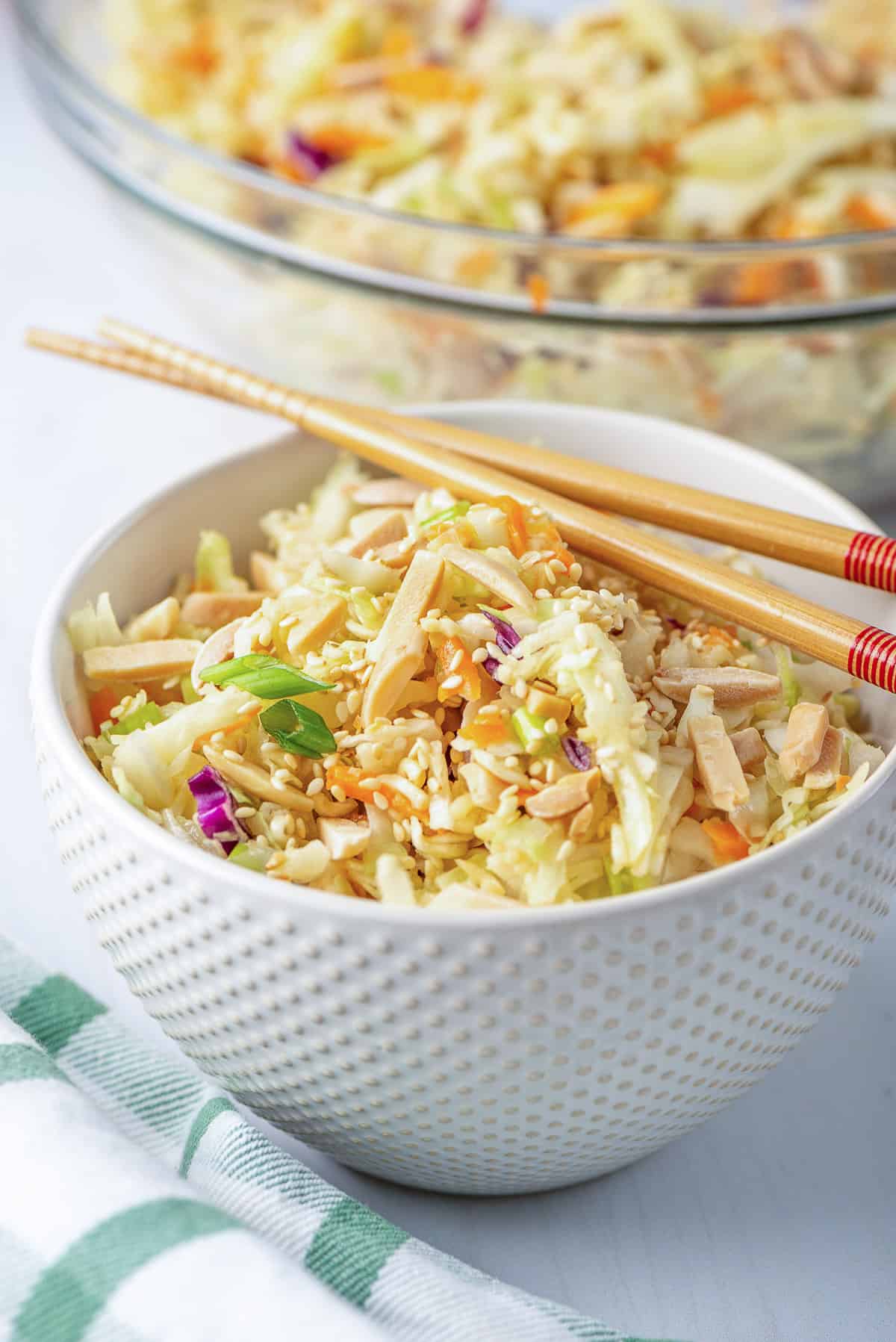 A white bowl filled with Ramen Cabbage Salad with chopsticks lying over the top.