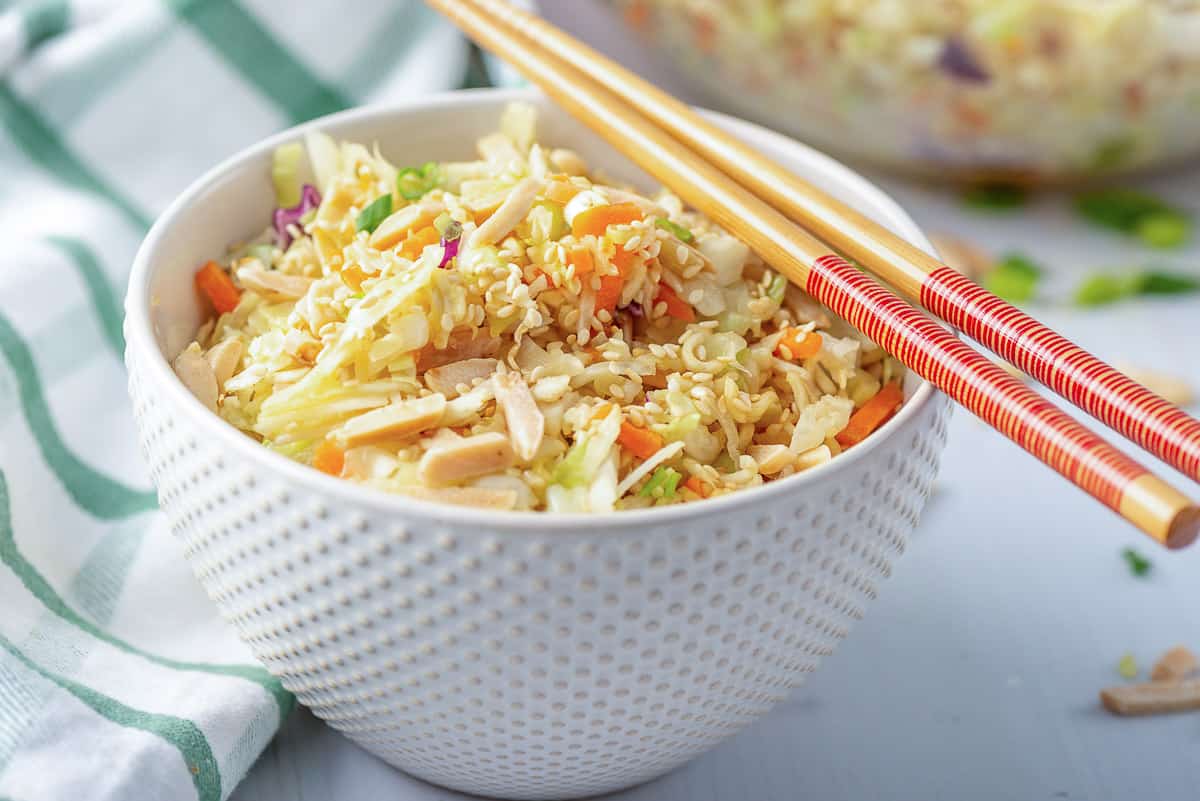 A white serving bowl filled with Ramen Cabbage Salad with chopsticks lying over the top.