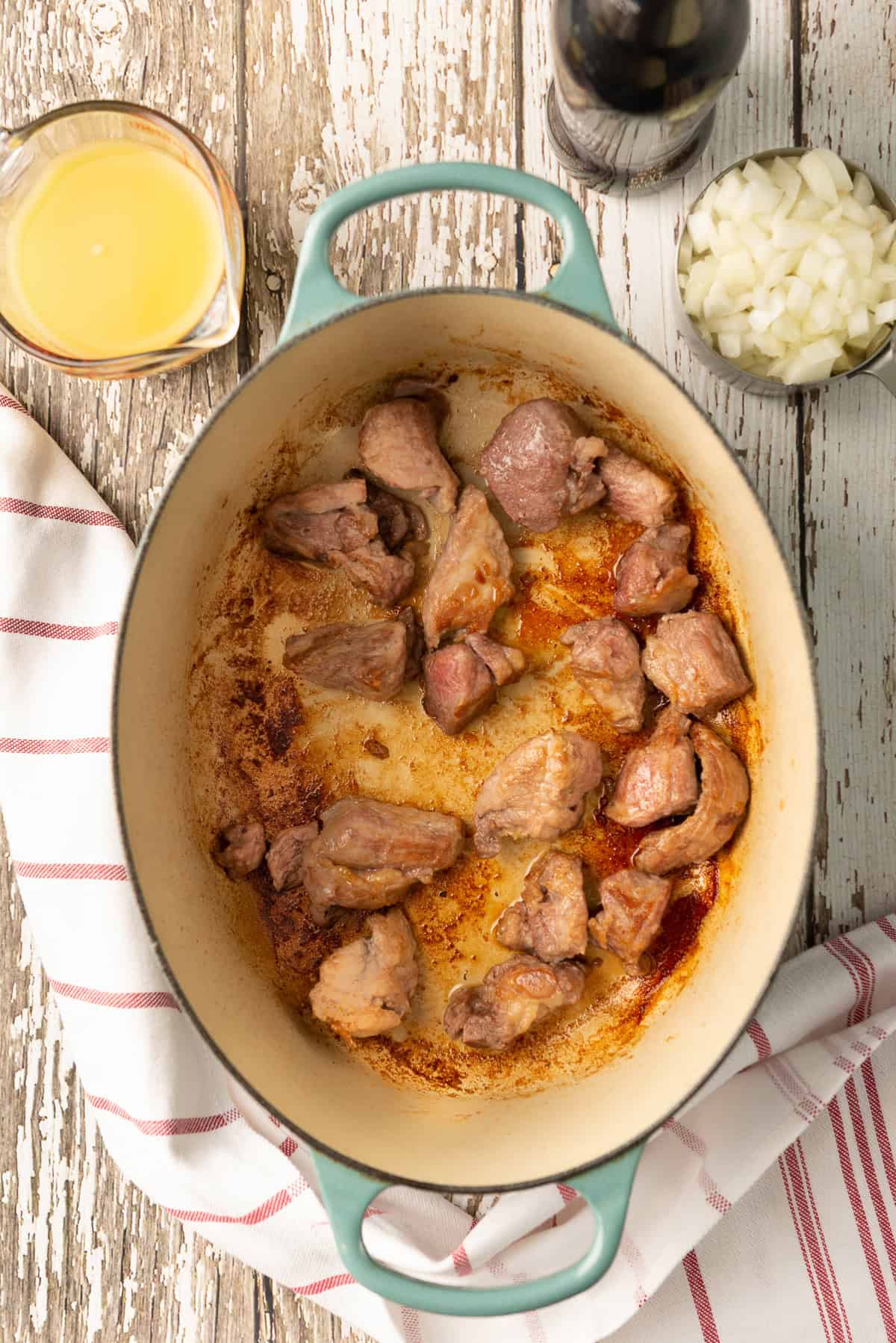 Pork pieces browning in a Dutch oven with browned bits on the bottom.