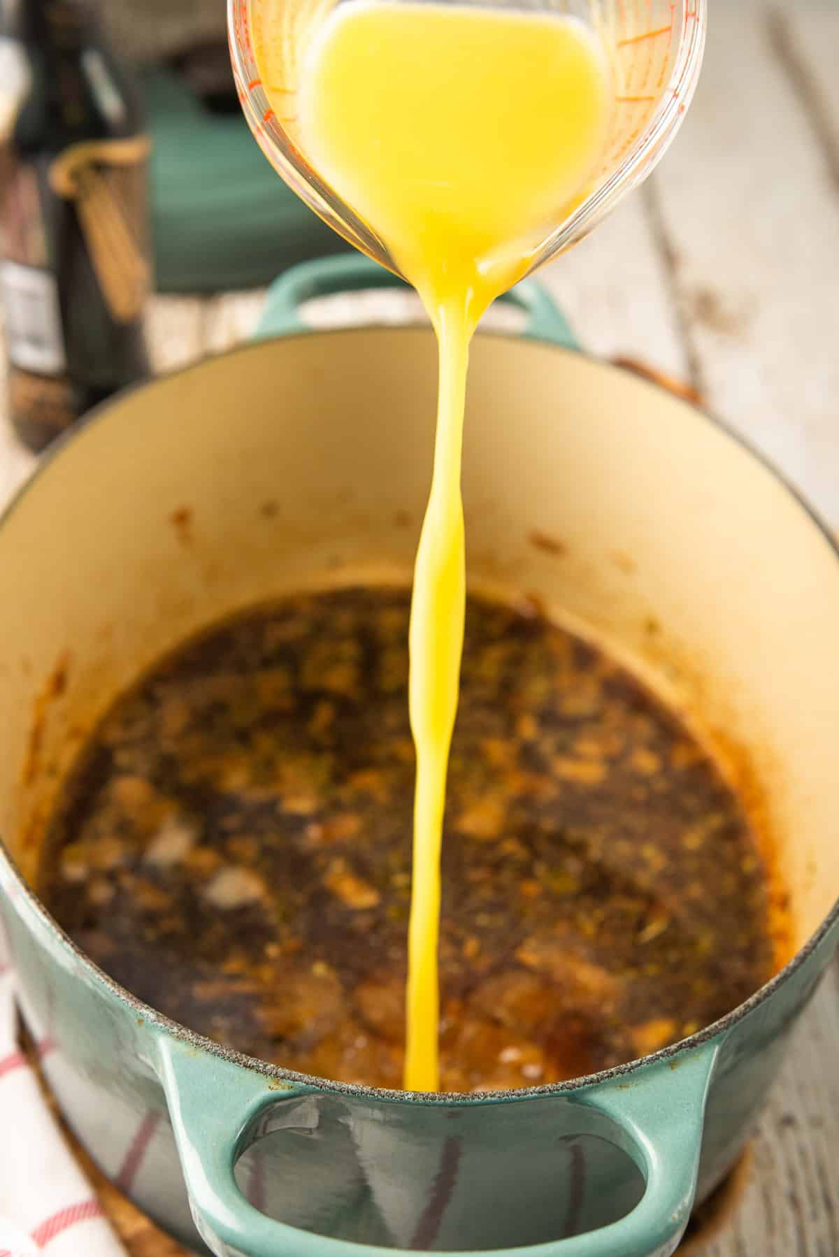 Fresh orange juice being added to the pot with the cooking liquid.