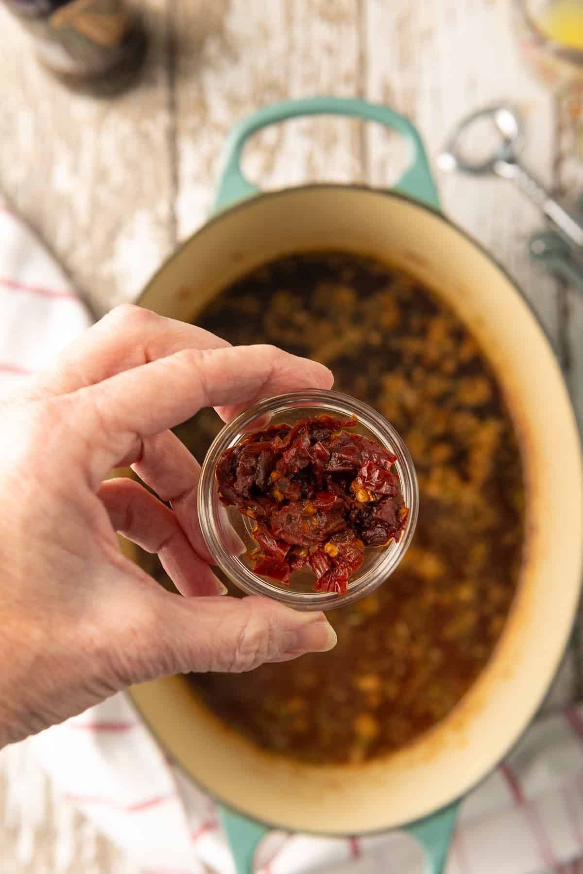 Chopped chipotle peppers in adobo sauce held above the pot.