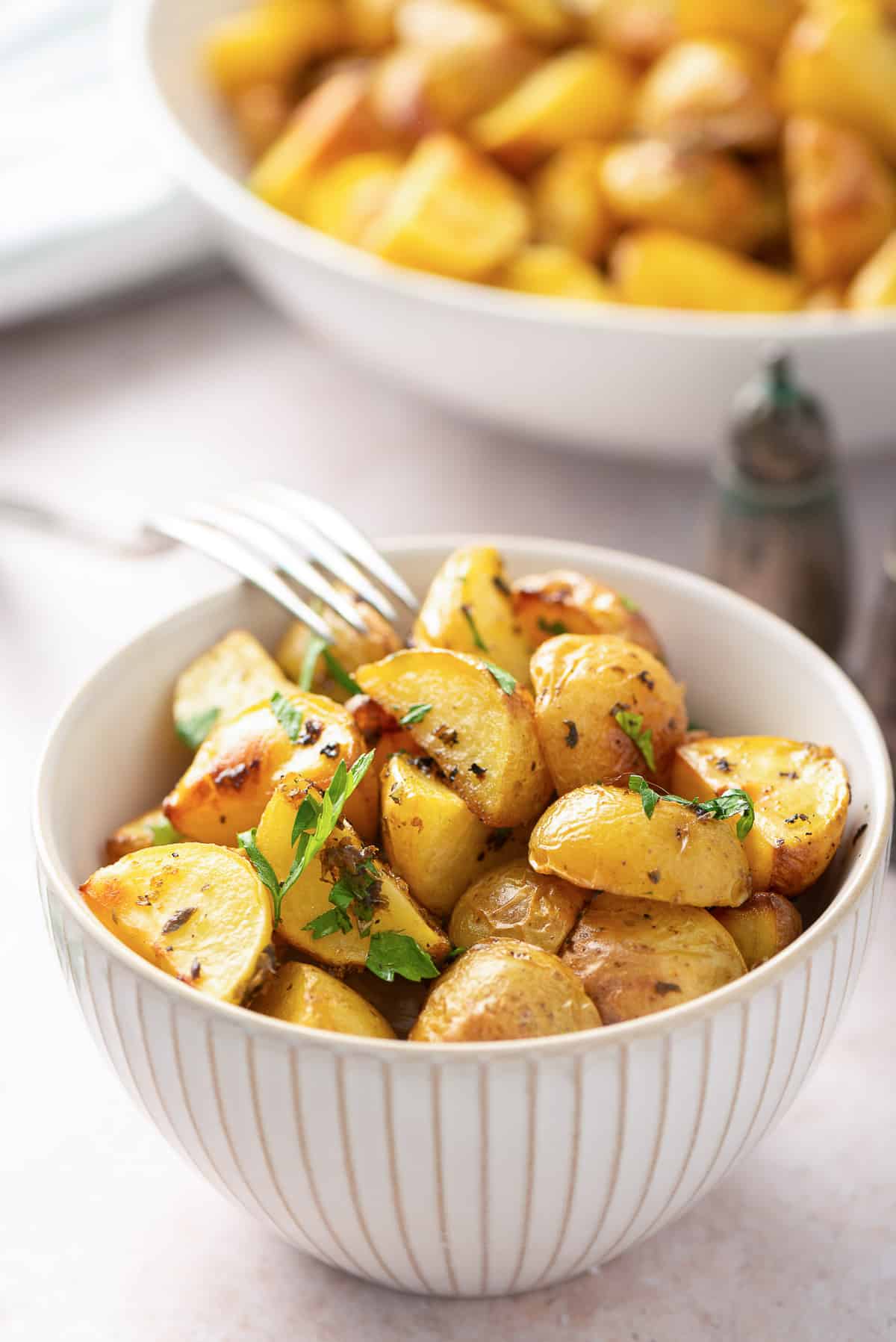 A small white bowl filled with Greek Potatoes.