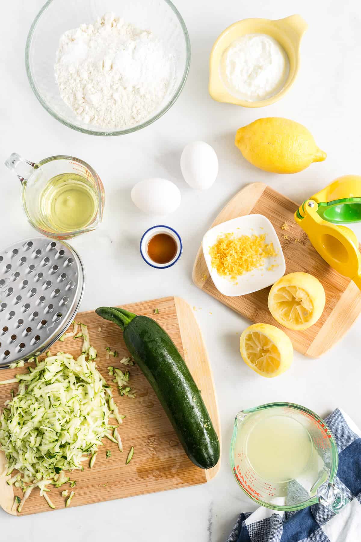 Lemon, zucchini, oil and other ingredients on a white counter.