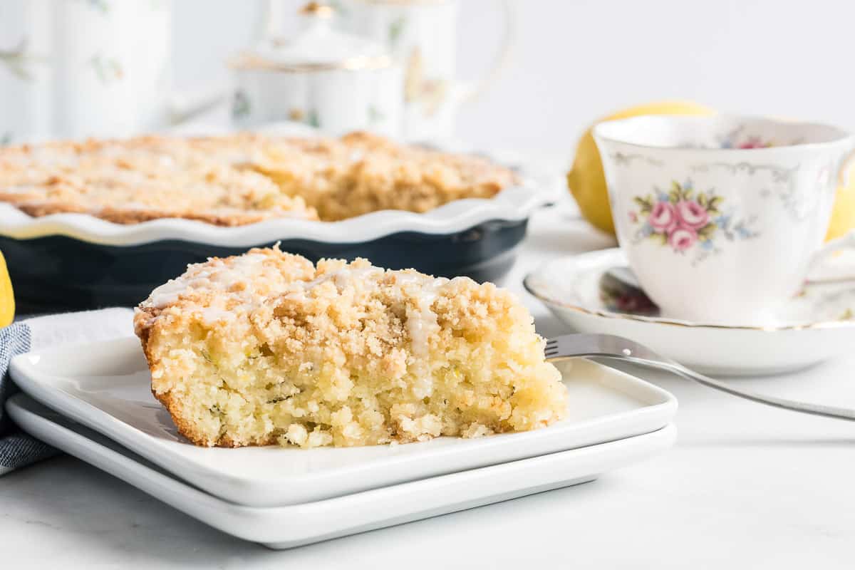 A slice of Lemon Zucchini Coffee Cake on a white place next to a tea cup.