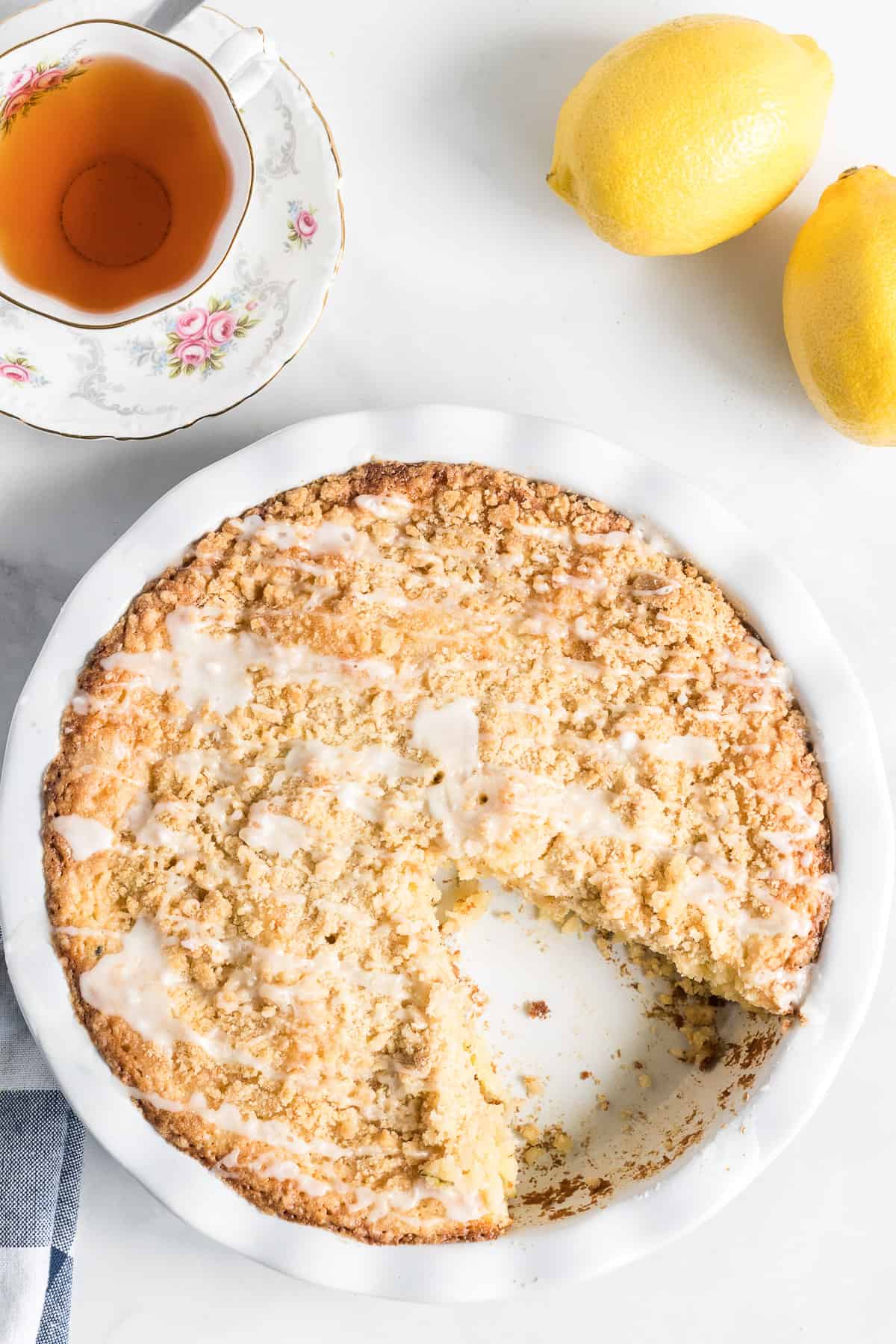 Lemon Zucchini Coffee Cake in a round baking dish with a cup of tea in the background.