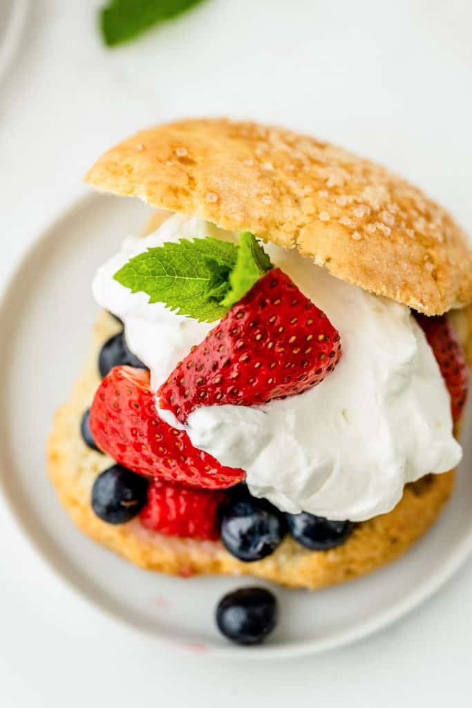 A close up of shortcake stuffed with berries and whipped cream on a white plate.