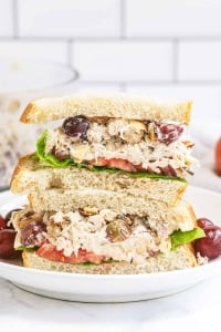 A Napa Almond Chicken Salad Sandwich sliced in half and stacked on a plate with grapes.