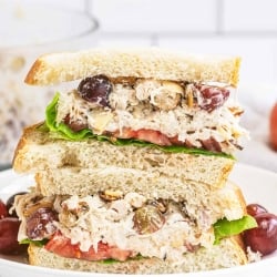 A Napa Almond Chicken Salad Sandwich sliced in half and stacked on a plate with grapes.
