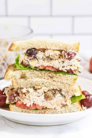 A Napa Almond Chicken Salad Sandwich sliced in half and stacked on a plate with grapes.