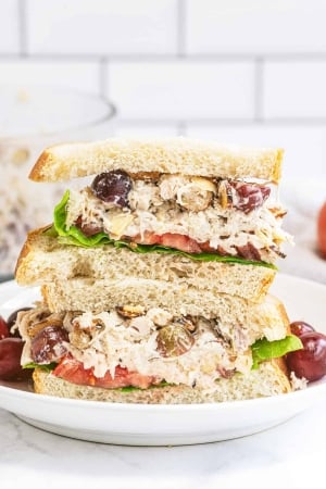 A Napa Almond Chicken Salad Sandwich sliced in half and stacked on a plate with grapes.