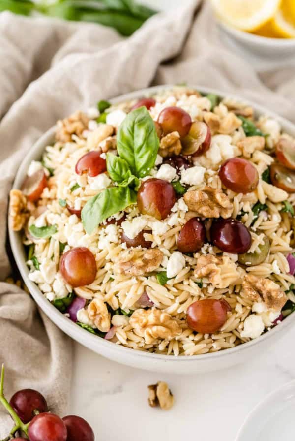 The orzo pasta salad in a white serving bowl with grapes and lemons placed around it.