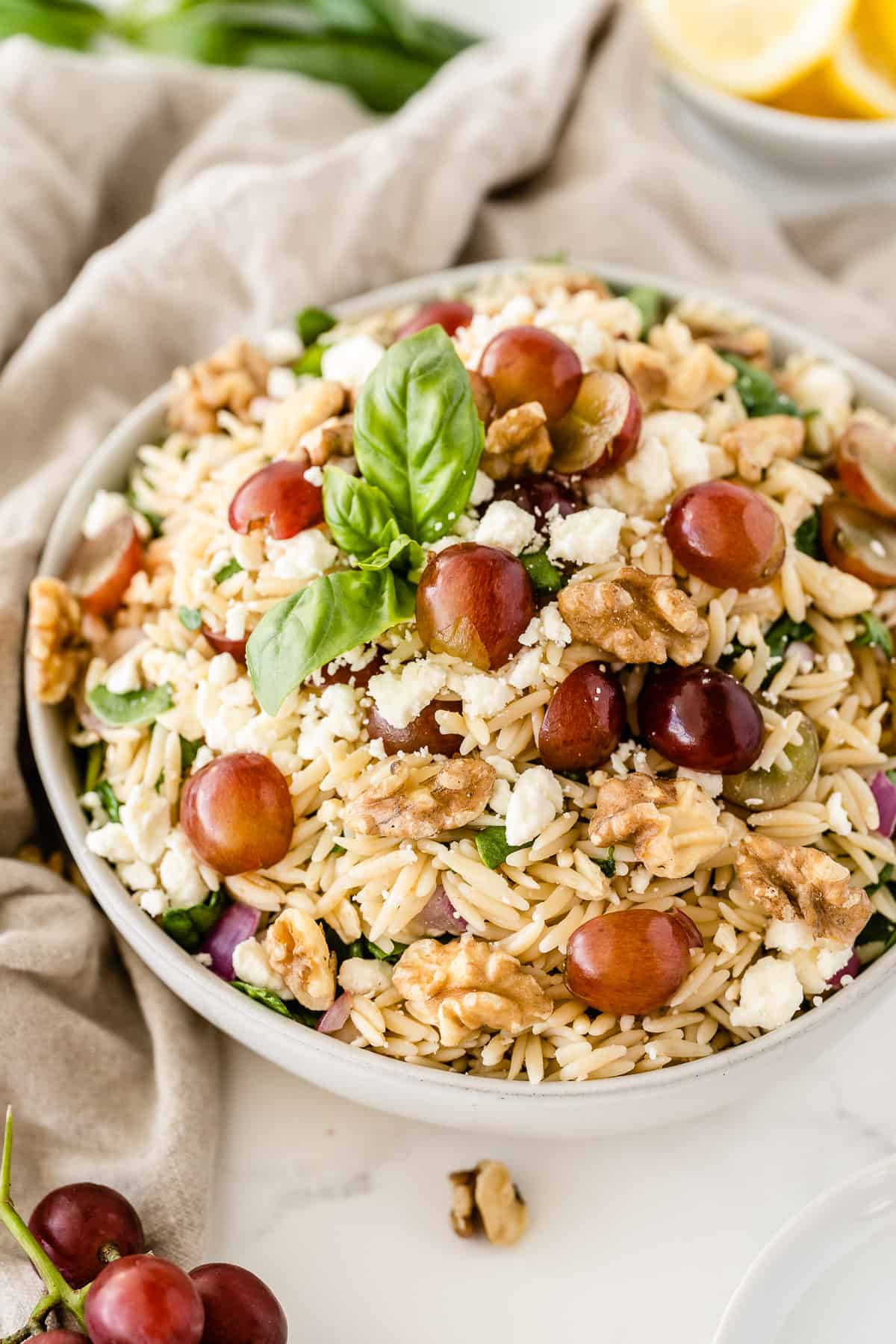 The orzo pasta salad in a white serving bowl with grapes and lemons placed around it.