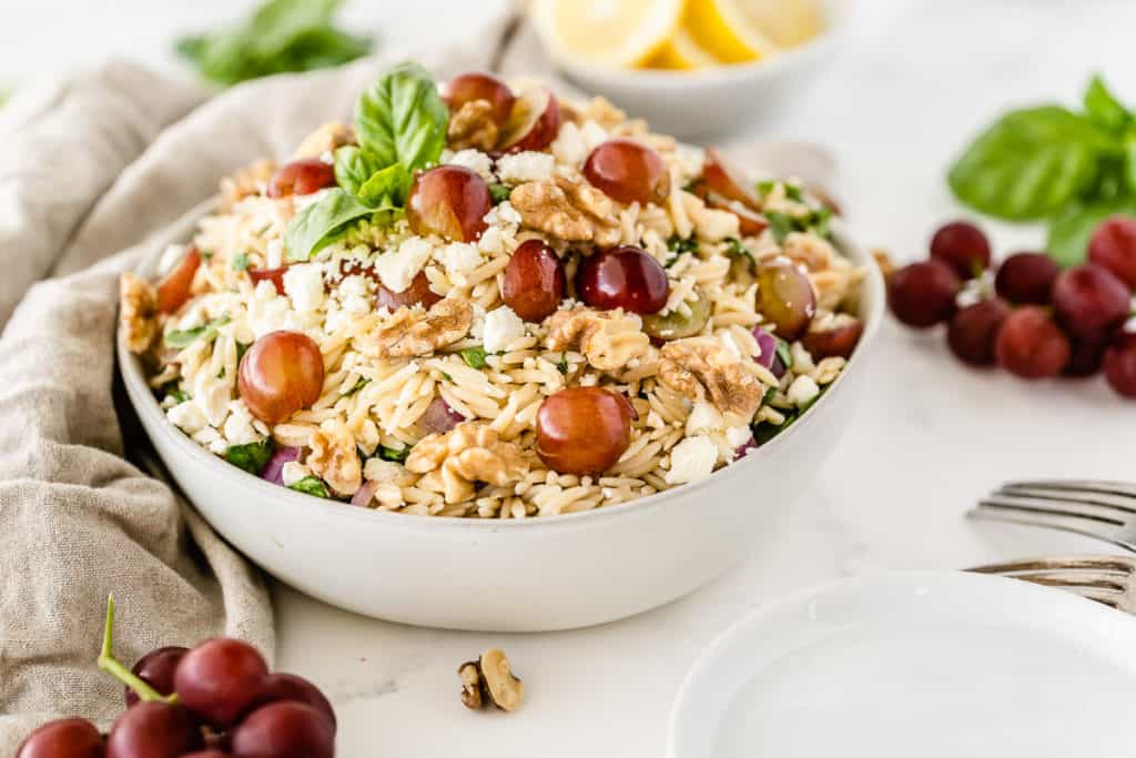 Orzo Grape Feta Salad in a white serving bowl with grapes set around it.