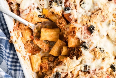 A spoon digs in to the center of the Pizza Pasta in a white casserole dish.
