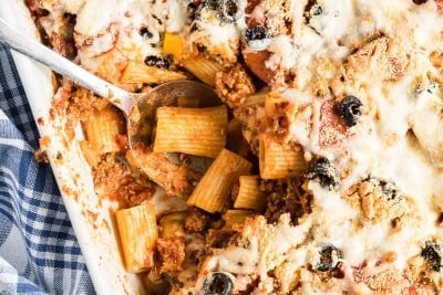 A spoon digs in to the center of the Pizza Pasta in a white casserole dish.