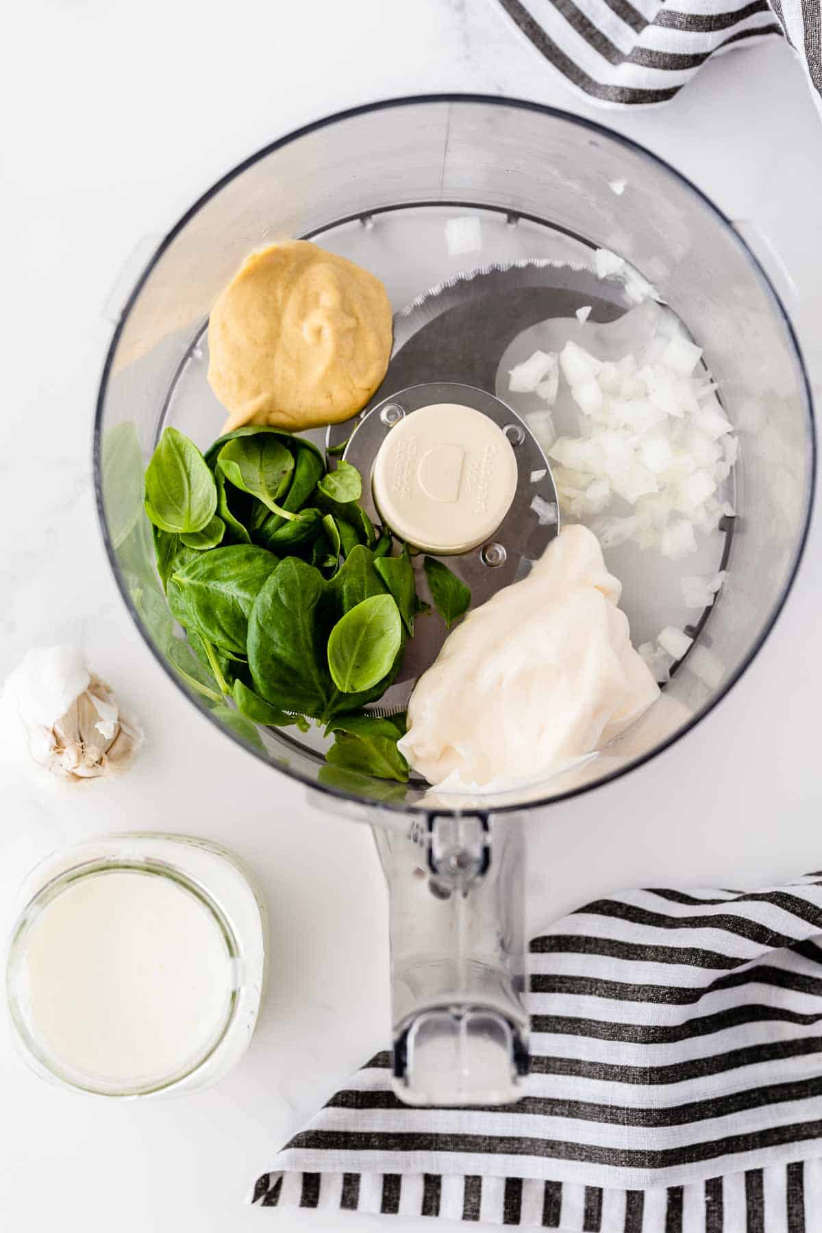 All the ingredients required to make Basil Buttermilk Dressing in the bowl of a food processor.
