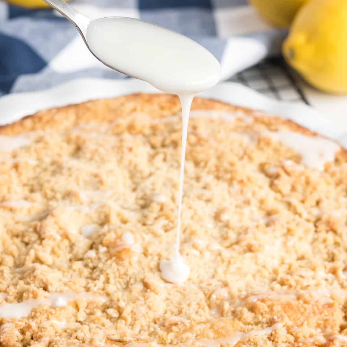 Lemon glaze being drizzled over baked lemon zucchini coffee cake with a crumb topping.