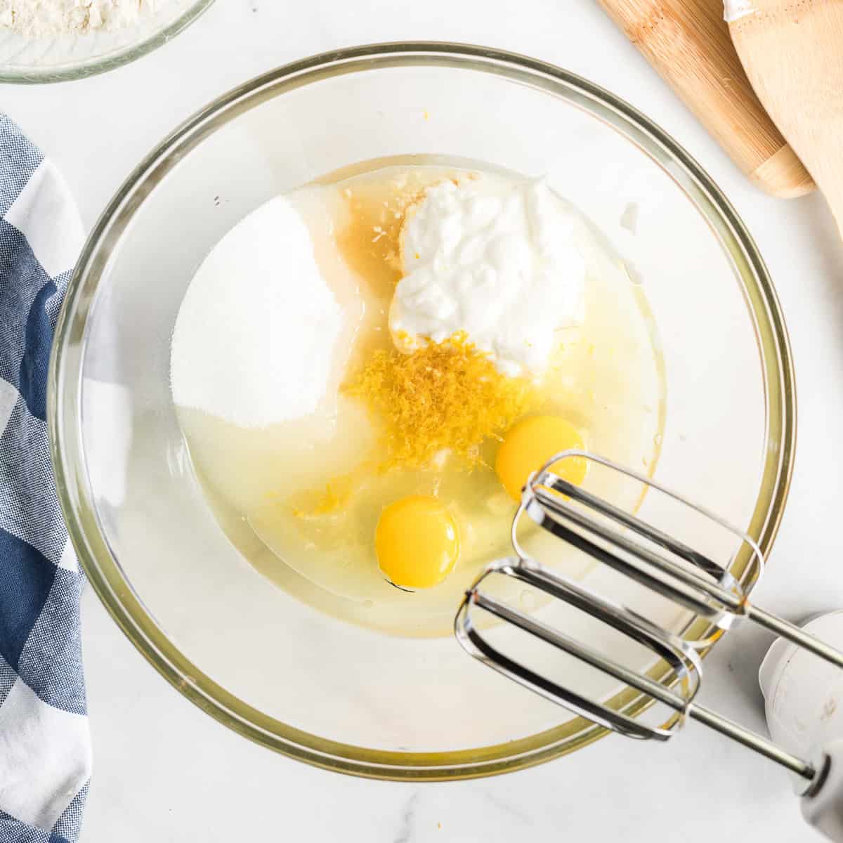 Wet ingredients for lemon zucchini coffee cake, including sugar, eggs, yogurt, oil, vanilla, and lemon zest, combined in a mixing bowl.