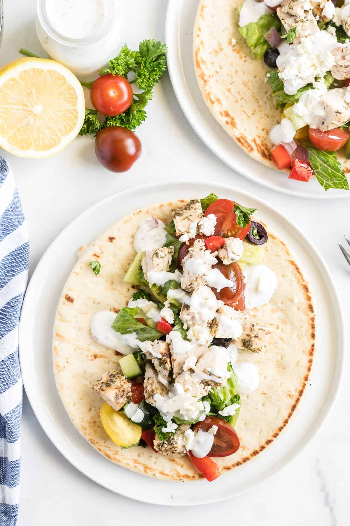 A pita on a plate layered with lettuce, vegetables, and grilled Greek chicken.