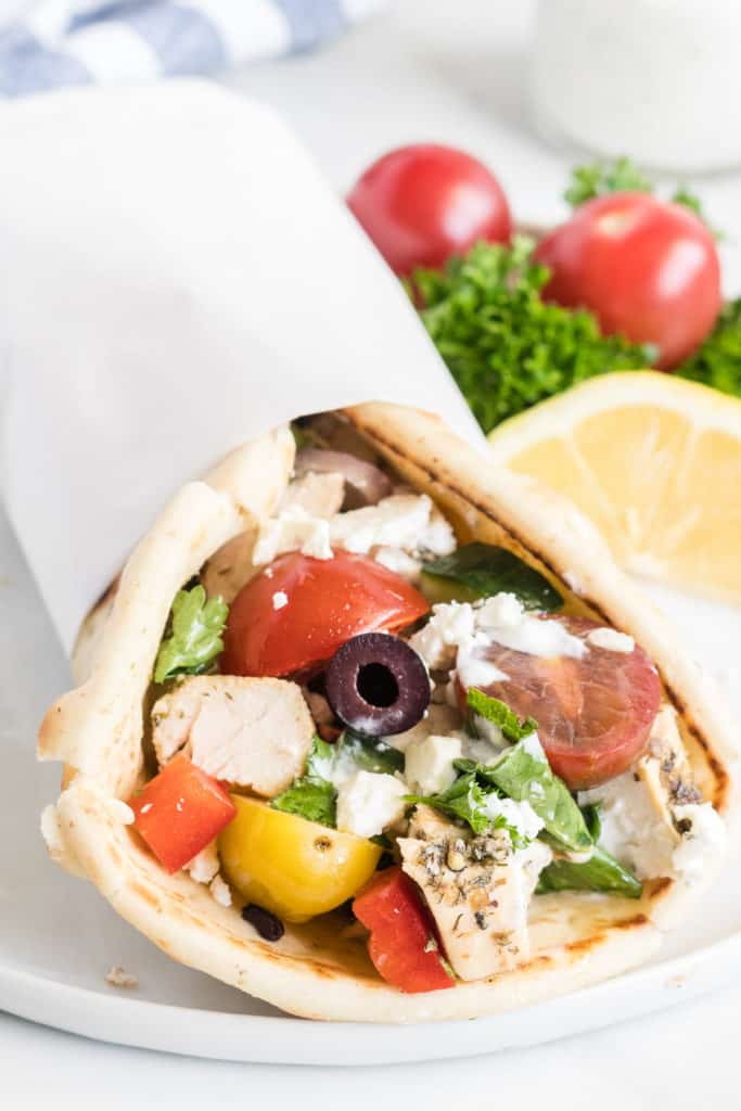 Chicken and a greek salad mixture stuffed in a pita and wrapped in parchment paper.