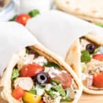 Two pitas stuffed with chicken and greek salad and wrapped in parchment paper.