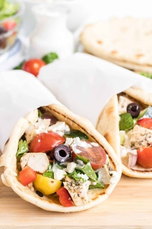 Two pitas stuffed with chicken and greek salad and wrapped in parchment paper.