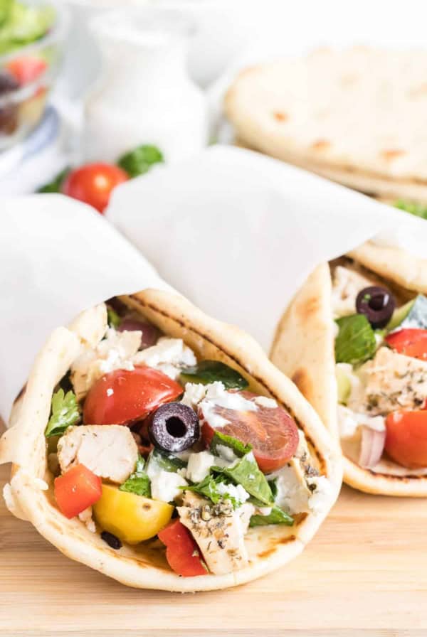 Two pitas stuffed with chicken and greek salad and wrapped in parchment paper.