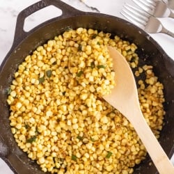 Corn being stirred with a wooden spoon in a cast iron skillet.
