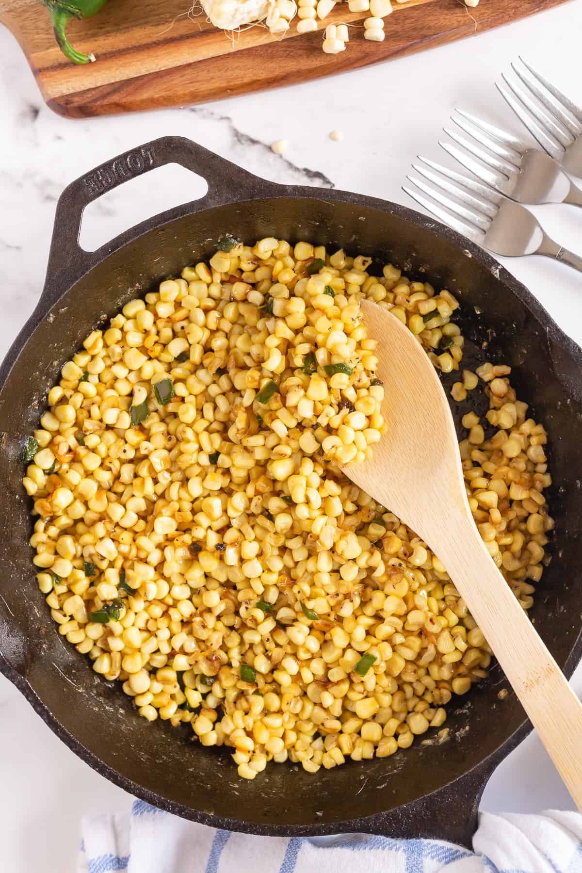 Corn being stirred with a wooden spoon in a cast iron skillet.