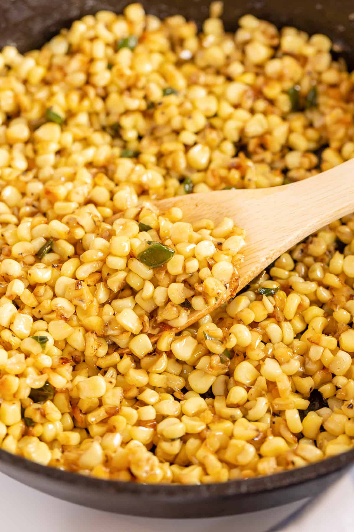 Corn being stirred with a wooden spoon in a cast iron skillet.