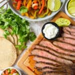 Sliced steak on a cutting board next to a bowl of bell peppers and onions.