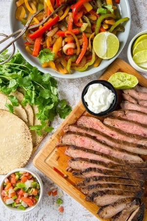 Sliced steak on a cutting board next to a bowl of bell peppers and onions.