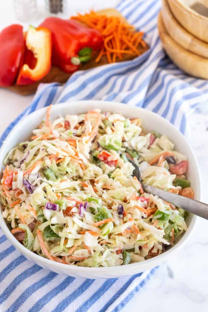 A white bowl filled with coleslaw with a spoon.