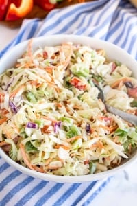 A white bowl filled with coleslaw with a spoon.