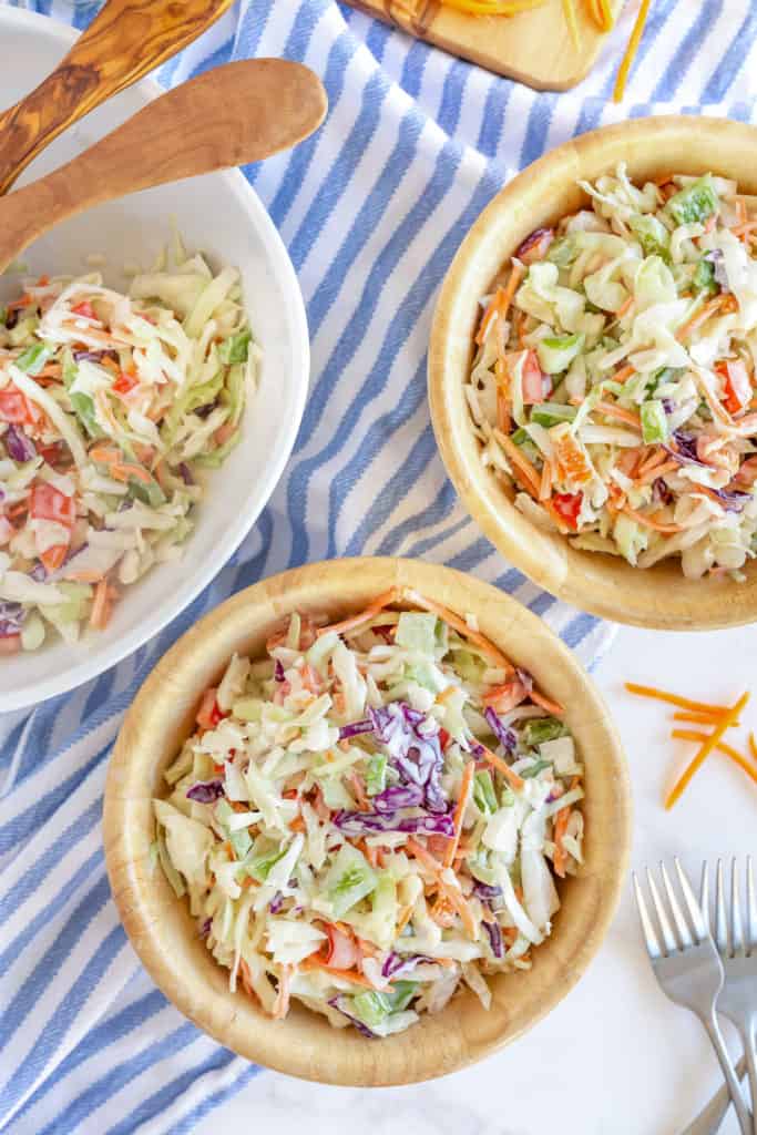 Two small wooden bowls filled with coleslaw on a blue a white striped cloth.