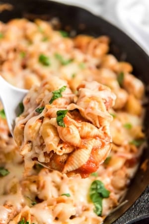 A spoon scoops Chicken Parmesan Pasta from a skillet.