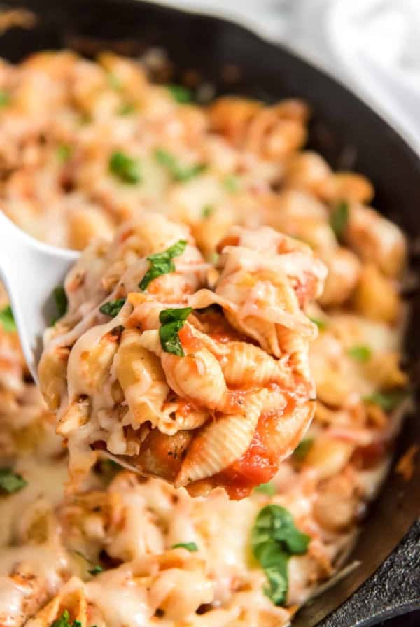 A spoon scoops Chicken Parmesan Pasta from a skillet.
