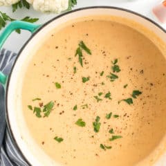 A pot full of Cauliflower Soup garnished with parsley.