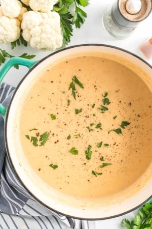 A pot full of Cauliflower Soup garnished with parsley.