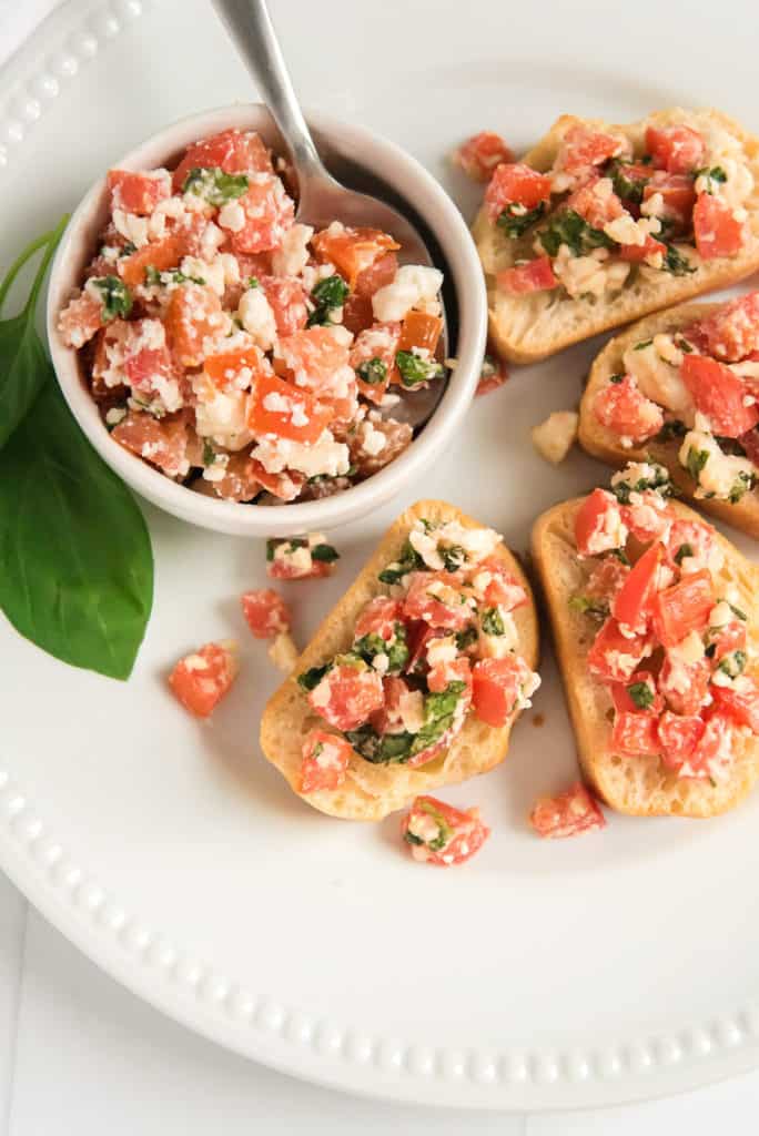 Sliced baguette topped with tomatoes and feta on a white plate.