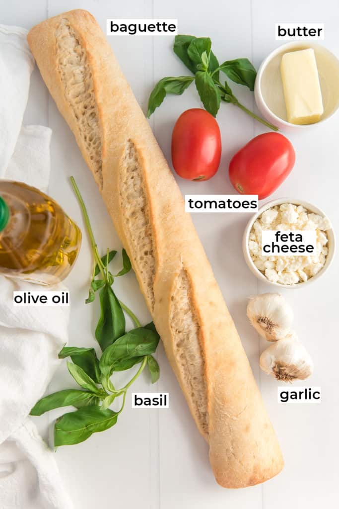 A baguette, tomatoes and other ingredients on a white surface with text overlay.